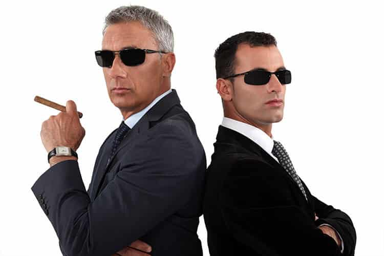 Two FBI agents back-to-back, wearing black suits and dark sunglasses