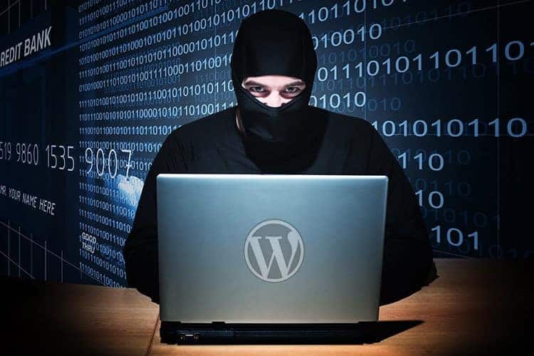 A hacker in black disguise sitting at a laptop against a dark backdrop with ones and zeros